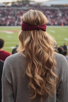 Woman with long wavy hair and red headband watching a football game.