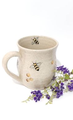 a mug with two bees on it next to some purple flowers