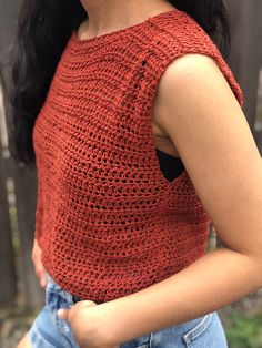 a close up of a woman wearing an orange top and denim shorts with her hands in her pockets