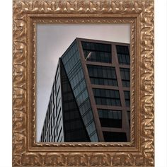 a framed photograph of a tall building in front of a cloudy sky with gold frame