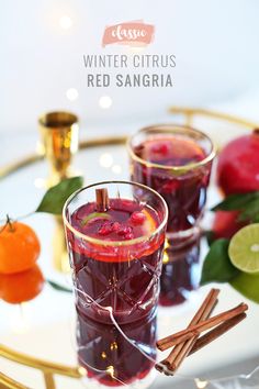 two glasses filled with red sangria sitting on top of a white plate next to oranges