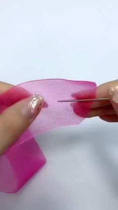 someone using scissors to cut pink ribbon on a piece of paper with nail polishing