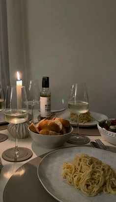 the table is set with wine, pasta and bread for two people to enjoy their meal