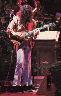 an image of a man that is playing the guitar on stage with other musicians in the background