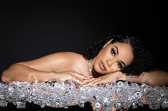 a beautiful woman laying on top of a pile of ice cubes in front of a black background