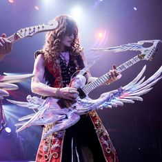 a woman with an electric guitar in her hand and wings around her neck, on stage