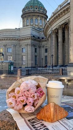 a cup of coffee and croissant sitting on a newspaper in front of a building