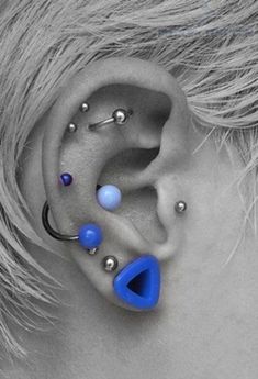 an ear with piercings on it is shown in black and blue colors, as well as silver balls