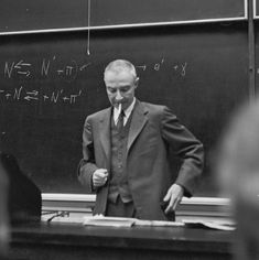 a man standing in front of a blackboard with writing on it and wearing a suit