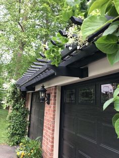 a house with a black garage door and green plants growing on the side of it