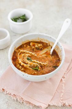 a bowl of soup with noodles and meat in it on a pink napkin next to two bowls