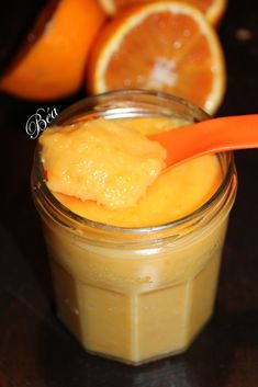 a glass jar filled with orange curd next to sliced oranges