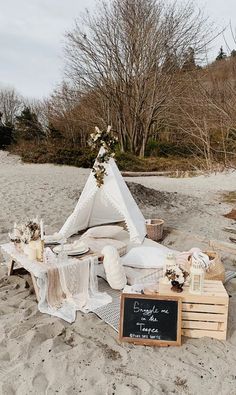 a teepee sitting on top of a sandy beach next to a chalkboard sign