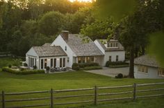 a large white house sitting in the middle of a lush green field next to a wooden fence