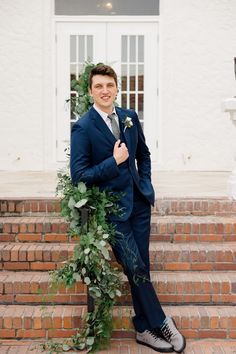 a man in a suit and tie standing on some steps with greenery around him