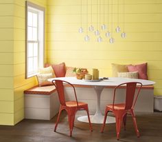 a white table with two red chairs next to a bench and yellow walls in a dining room