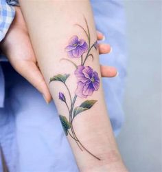 a woman's arm with purple flowers and leaves on the left side of her arm