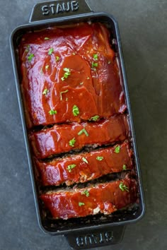 meatloaf with sauce and parsley in a black baking pan on a gray surface