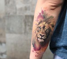 a man's arm with a lion tattoo on it and watercolor paint splatters