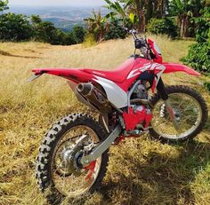 a red and white dirt bike parked on top of a grass covered field with trees in the background