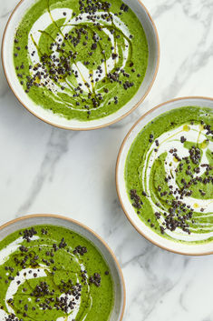 three bowls filled with green soup on top of a marble counter