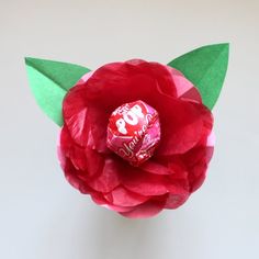 a candy bar wrapped in red tissue paper and sitting on top of a fake flower