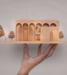 a hand is holding a model of a house on a shelf with trees in the background