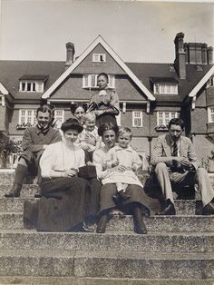 an old black and white photo of people sitting on steps in front of a house