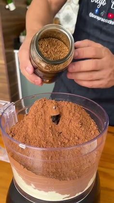 a person holding a jar filled with brown powder and ground cinnamon on top of a blender