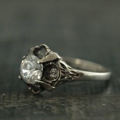 This stunning antique style ring is so romantic! It features sculptural flowers that surround and nestle the center 6mm stone. The stone is held in place by four prongs. You can choose a Cubic Zirconia or a White Topaz. Your ring will be made to size just for you and oxidized and polished for an antiqued look.Deb is a professional jeweler that has dedicated over 15 years to her craft. Please don't hesitate to contact us with any questions or concerns. All of our jewelry is hand made to order. We Engagement Ring Antique, Antique Style Rings, Quartz Engagement Ring, Black Engagement Ring, Black Stone Ring, Floral Engagement Ring, Cubic Zirconia Engagement Rings, Antique Wedding Rings, Silver Engagement Ring