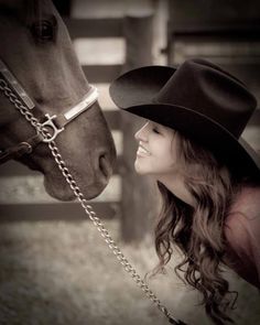 a woman wearing a cowboy hat standing next to a horse