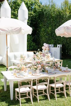 an outdoor table set up for a party with umbrellas and flowers in the grass