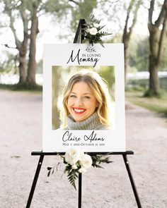 a white sign with flowers on it sitting in front of trees