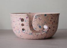 a ceramic bowl with holes and splattered paint on it's side, sitting on a table