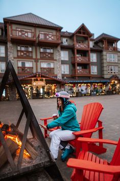 a woman sitting on red chairs next to a fire pit in front of a building