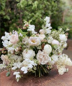 a bouquet of flowers sitting on top of a wooden table in front of some bushes