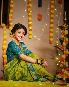 a woman sitting on the ground wearing a green sari and smiling at the camera