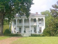 a large white house sitting in the middle of a lush green field next to trees