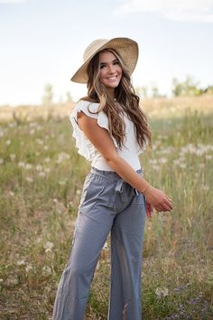 a woman standing in the middle of a field wearing a hat and wide legged pants