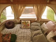 a bed sitting under a window in a room with curtains and pillows on top of it