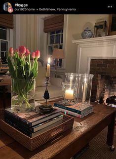 a table topped with books and candles next to a fire place in a living room