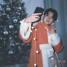 a young man taking a selfie with his cell phone in front of a christmas tree