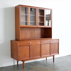 a wooden cabinet with glass doors on the top and bottom, against a white wall