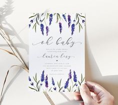 a person holding up a card with purple flowers and greenery on it, in front of a white background