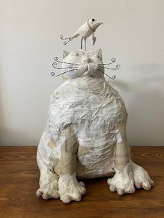 a cat statue sitting on top of a wooden table next to a bird perched on it