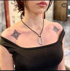 a woman with tattoos on her chest wearing a black top and necklace that has an arrow in the middle