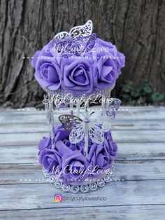 purple roses in a glass vase with butterflies on the top and some crystals hanging from it