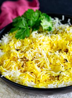 a black bowl filled with yellow rice and garnished with parsley