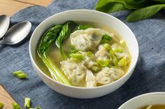 two bowls filled with soup on top of a blue cloth next to spoons and green leaves