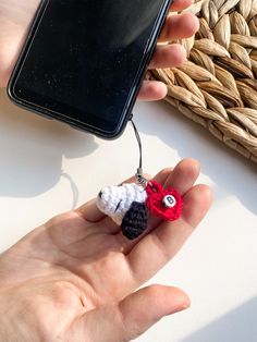 a hand holding a tiny crocheted ornament in front of a cell phone